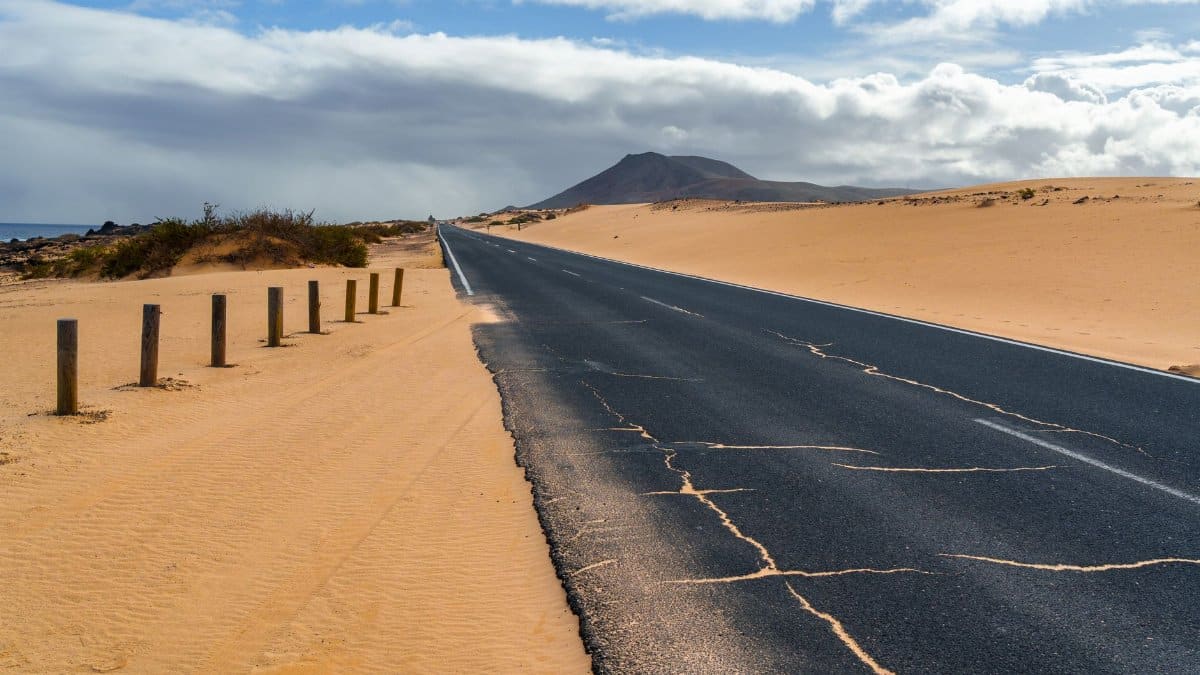 A long road stretches through a barren desert landscape towards a distant mountain.