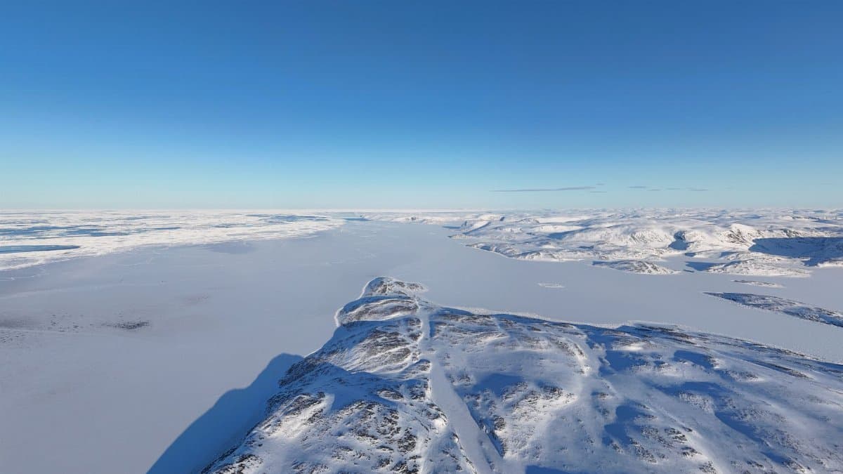 A breathtaking aerial view of a snow-covered mountain range under a clear blue sky, capturing winter wilderness.