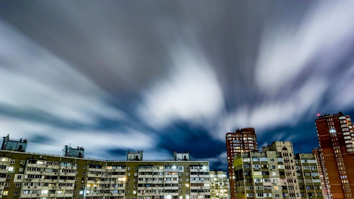 Long exposure of urban skyline with illuminated buildings and fast-moving clouds creating a dynamic city night scene.