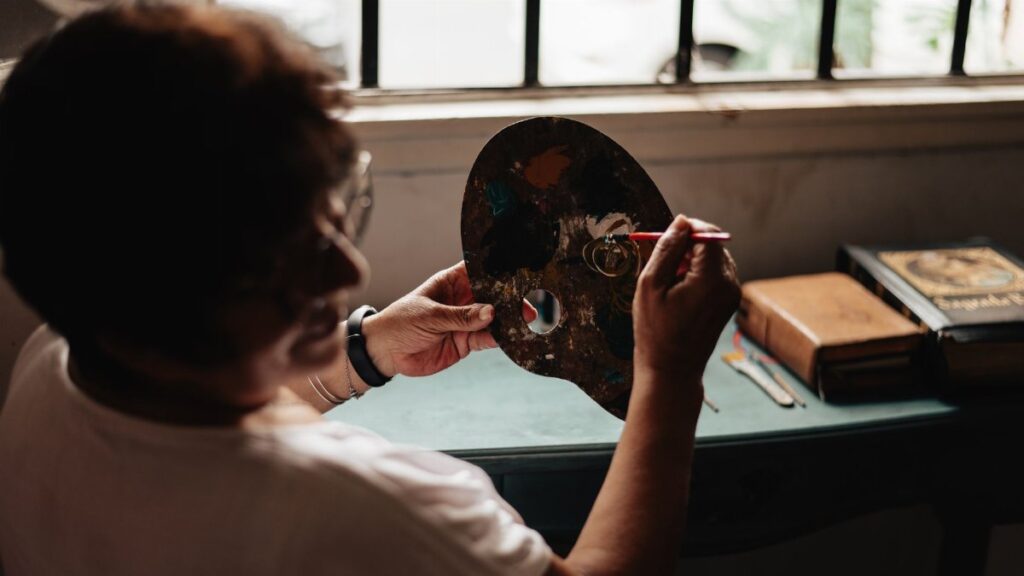 An adult painter works on a palette indoors, creating art by natural window light in Buenos Aires.