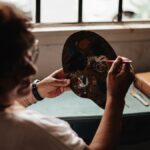 An adult painter works on a palette indoors, creating art by natural window light in Buenos Aires.