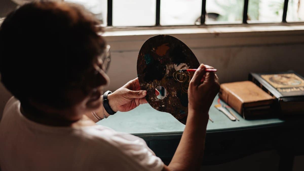 An adult painter works on a palette indoors, creating art by natural window light in Buenos Aires.