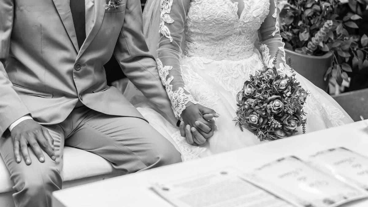 A newlywed couple's hands intertwined during their wedding ceremony, captured in black and white.