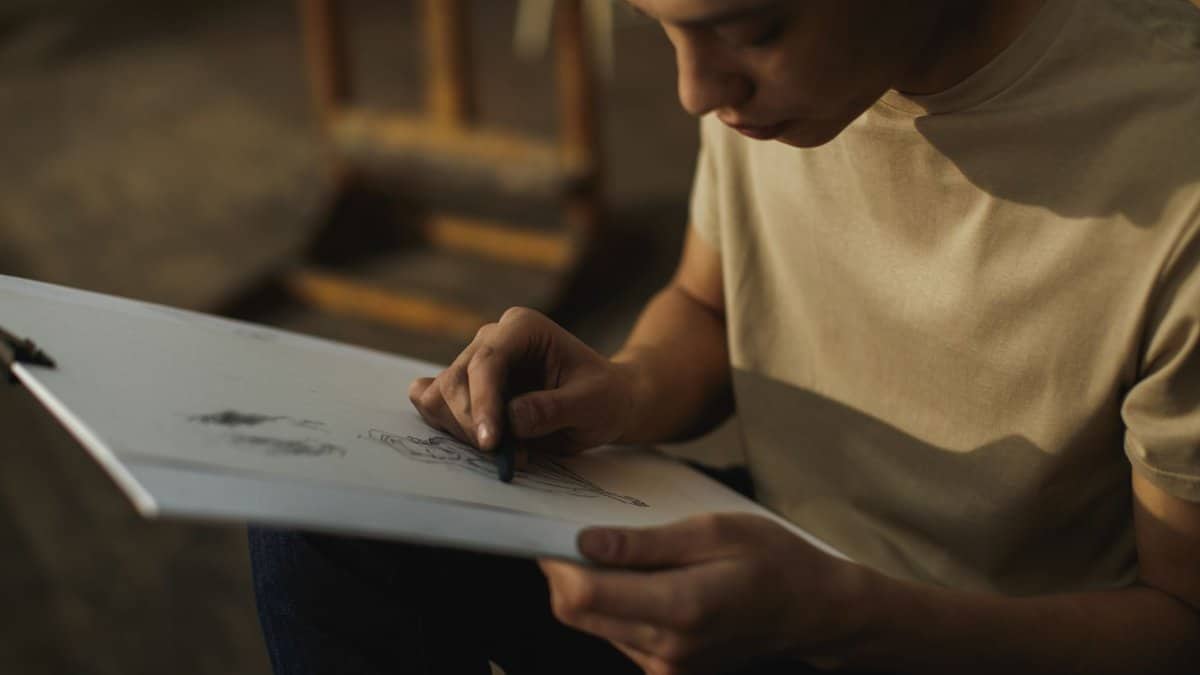 Focused adult drawing with charcoal on paper in an indoor art studio setting.