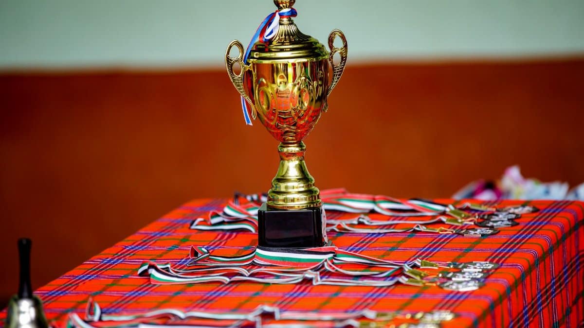 Golden trophy with ribbons and medals on a checkered table, symbolizing victory and achievement.