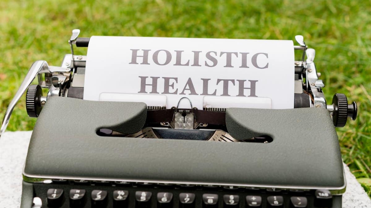 A vintage typewriter in a grassy outdoor setting displaying 'Holistic Health' on paper.