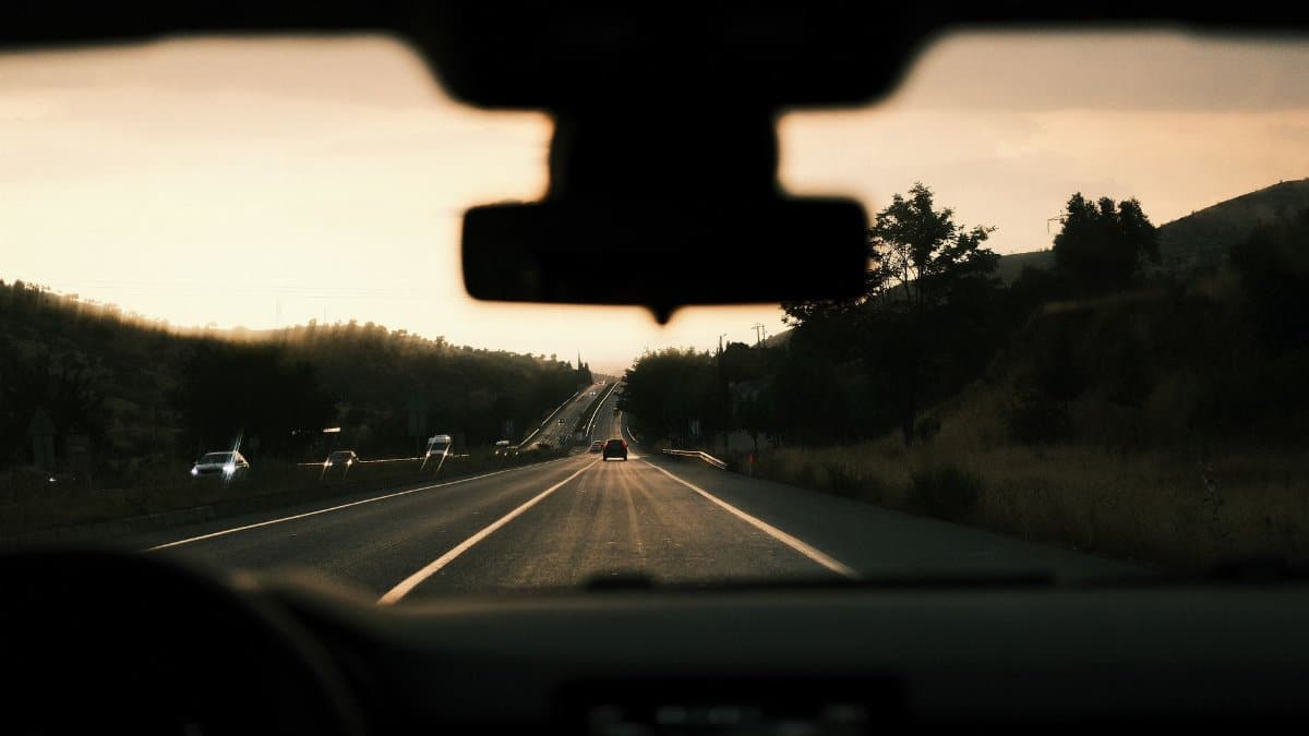 View through a car windshield of a scenic highway during sunset, capturing the road trip vibe.
