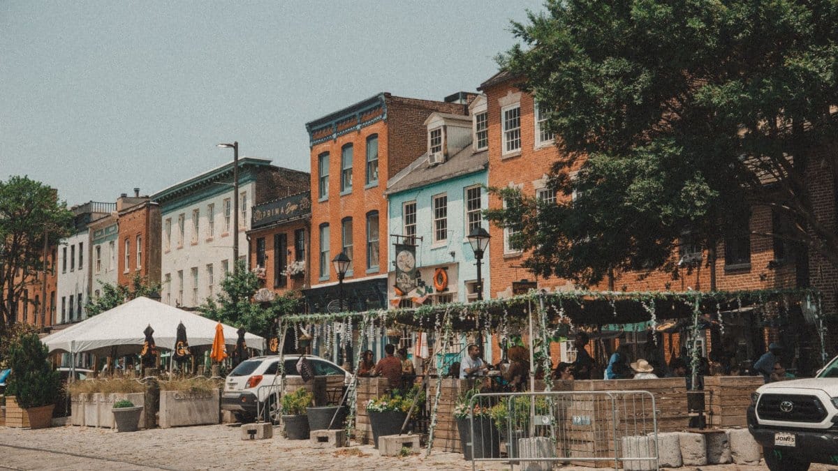 Vibrant street scene in Baltimore with colorful row houses, outdoor cafes, and bustling summer atmosphere.
