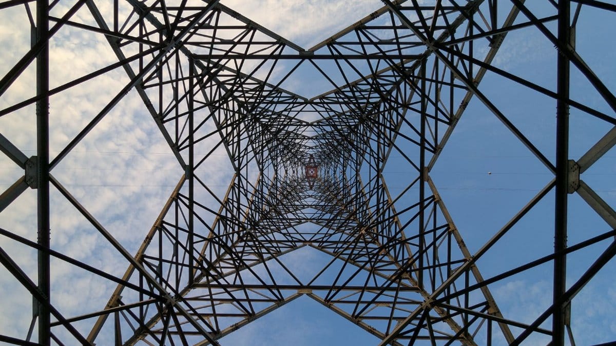 Looking up through a steel power tower against a blue sky and clouds.