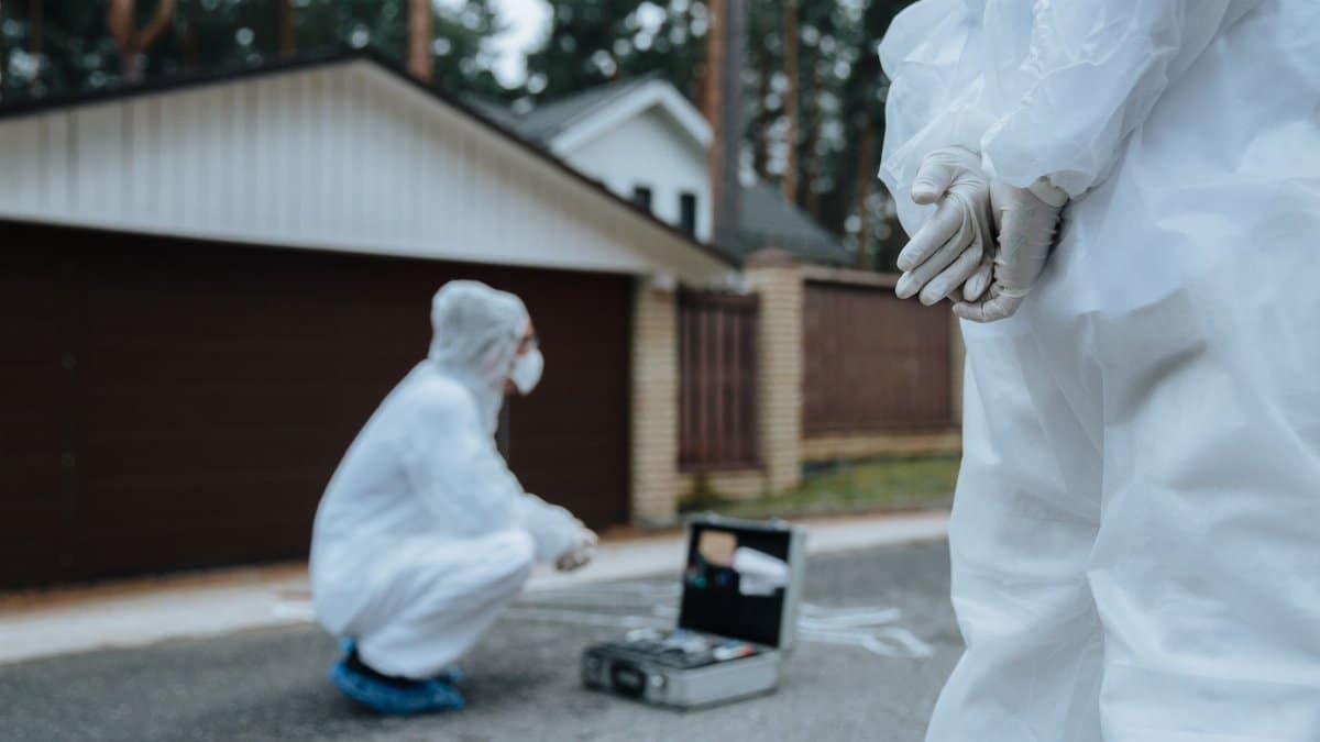 Forensic investigators in white suits and masks examining a crime scene outside a residential area.