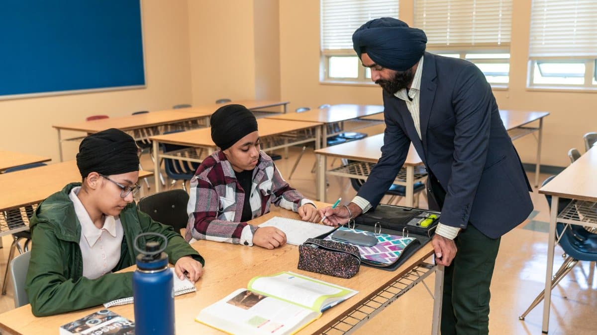 A teacher helps two students with homework in a bright classroom environment.