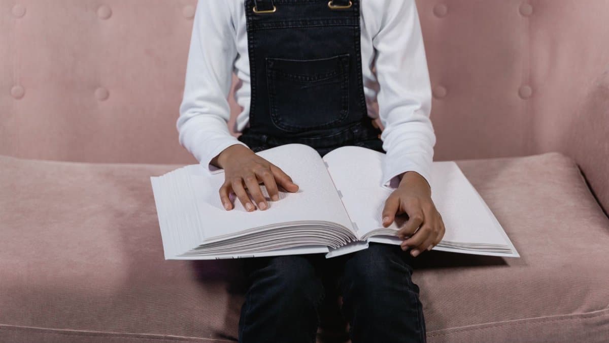 A child sits on a sofa holding and reading a Braille book, signifying learning and accessibility.