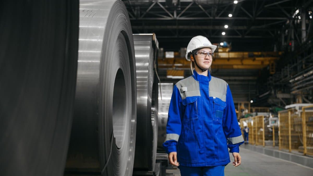 Female industrial worker in protective gear at a steel manufacturing facility.
