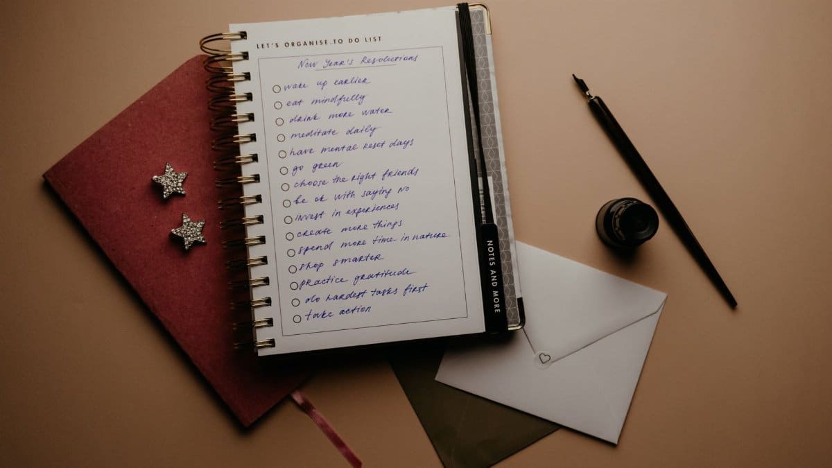 A detailed New Year's resolution to-do list in a notebook with writing materials.