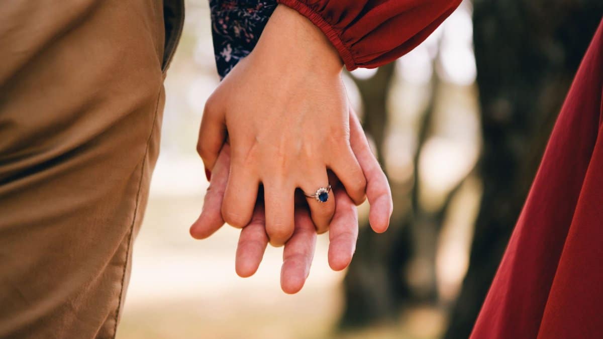 Close-up of a couple holding hands, highlighting an engagement ring in a romantic outdoor setting.