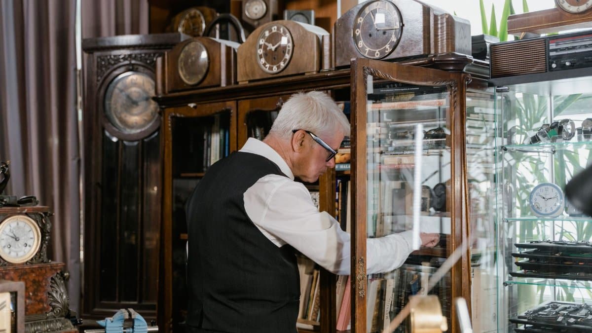 An older man examines clocks in a vintage shop filled with antique timepieces.
