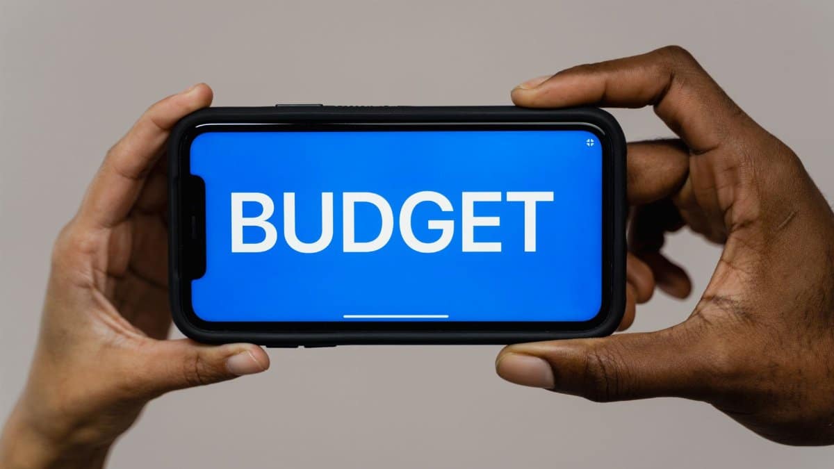 Two hands hold a smartphone displaying the word 'budget' on a blue screen, symbolizing financial planning.