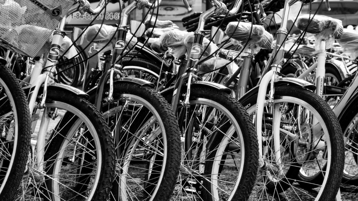Black and white image of parked vintage bicycles on a street, highlighting spokes and handlebars.