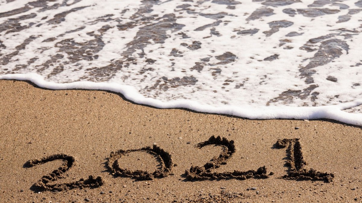 Beach scene with 2021 written in sand as ocean waves approach, symbolizing new beginnings.
