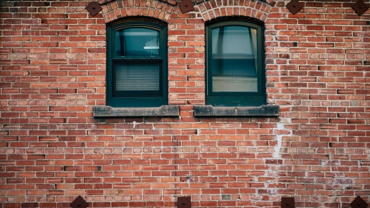 Closed green windows with jalousie of old weathered building with red brick wall during daytime
