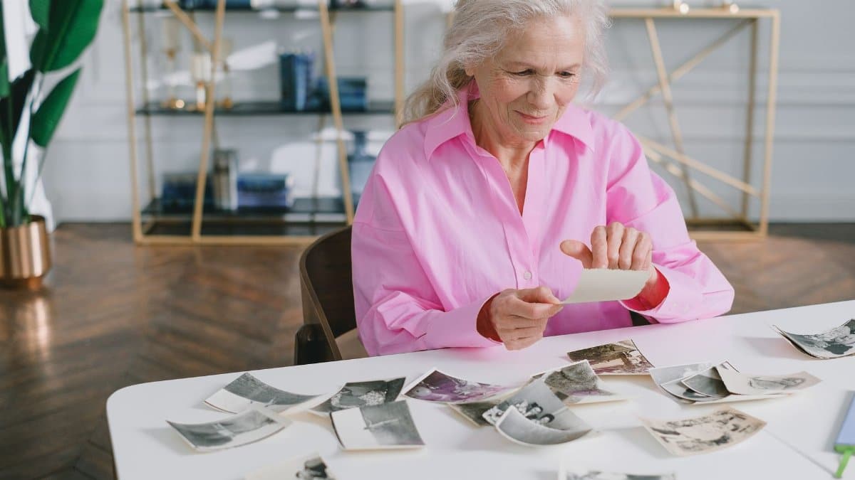 A senior woman reliving past memories by looking through old photographs at a table.