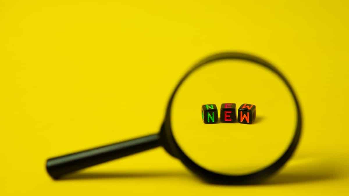 Concept image of big black magnifier with word new in form of cubes against yellow background