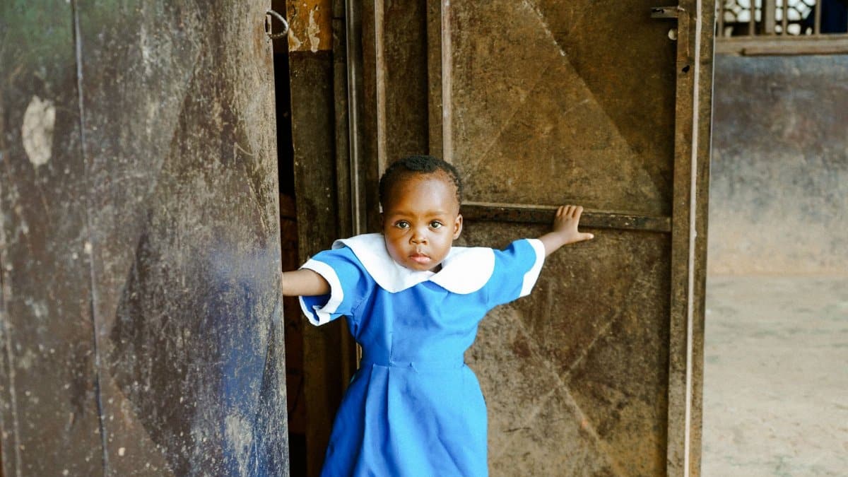 A young child in a blue school uniform standing in a doorway, looking curious.