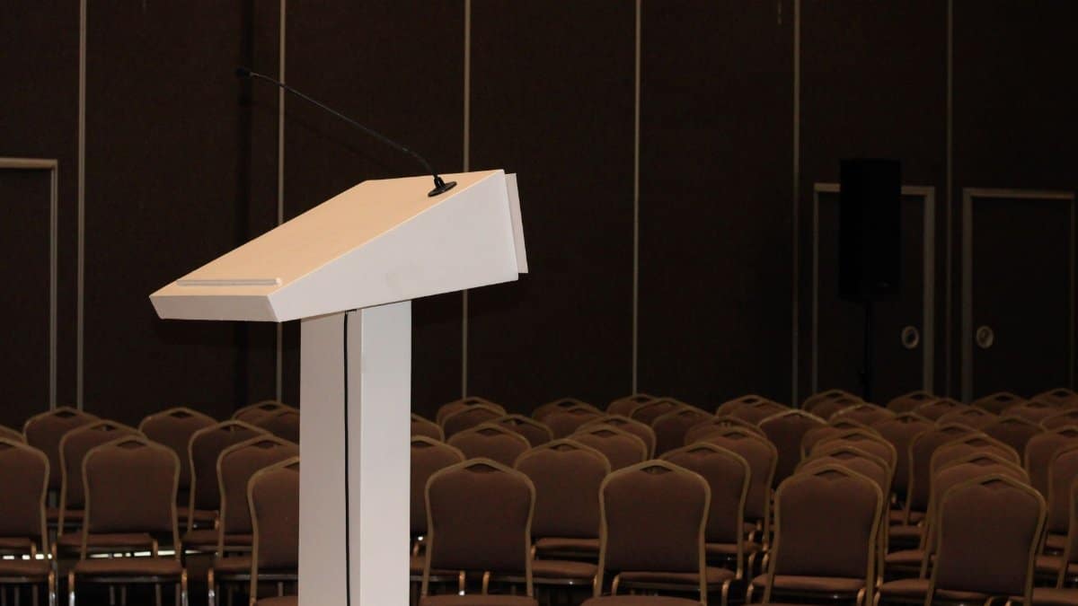 An empty conference room setup with podium and rows of chairs, ready for an event.