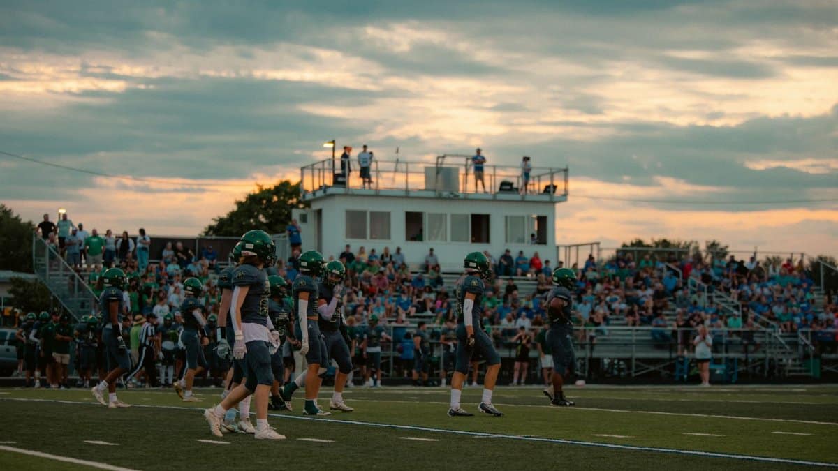 Football players and crowd in a stadium during a sunset game.