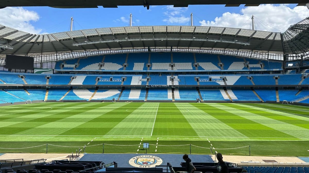 Panoramic view of Etihad Stadium, showcasing the empty football pitch and stands under a clear blue sky.