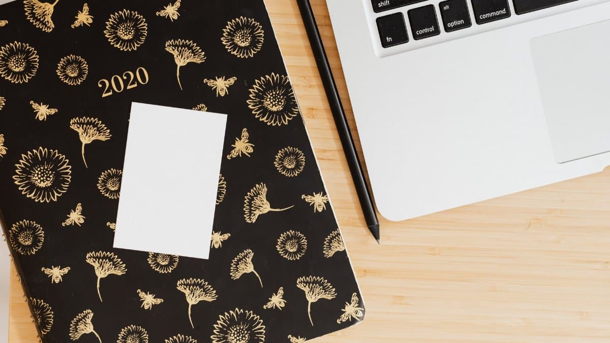Top view of a modern workspace featuring a floral planner, pen, and laptop on a wooden desk.