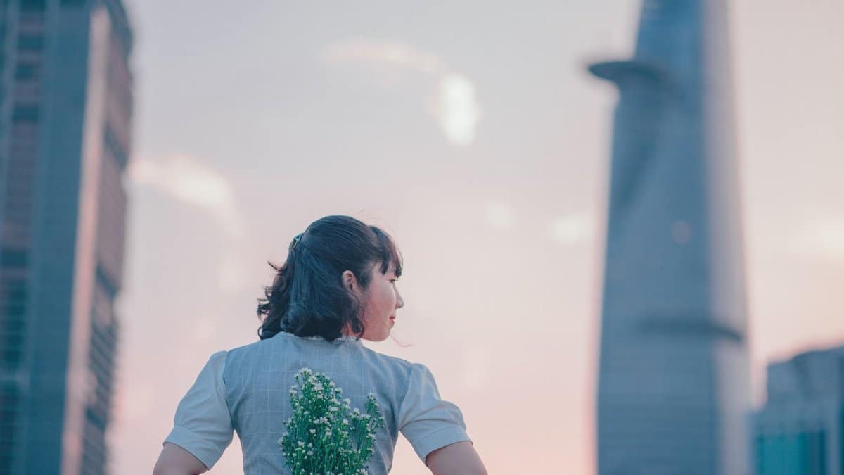 Woman with flowers in a cityscape at sunset, blending nature with modern architecture.
