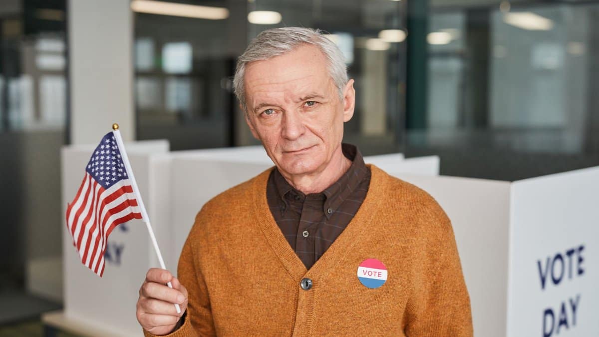 Elderly man with American flag and vote sticker in polling station. Emphasizing civic duty and participation.