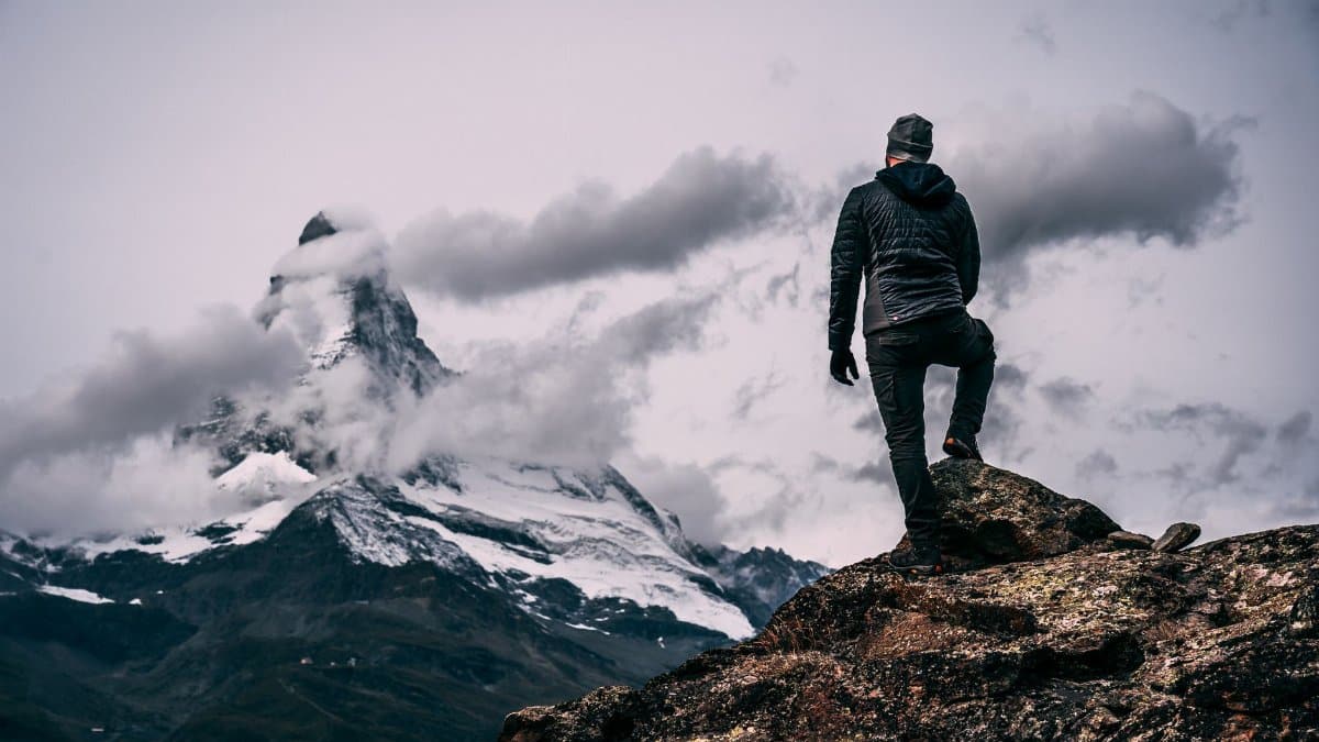 Back view of a man hiking on rocky terrain with a snowy mountain ahead, set in winter.