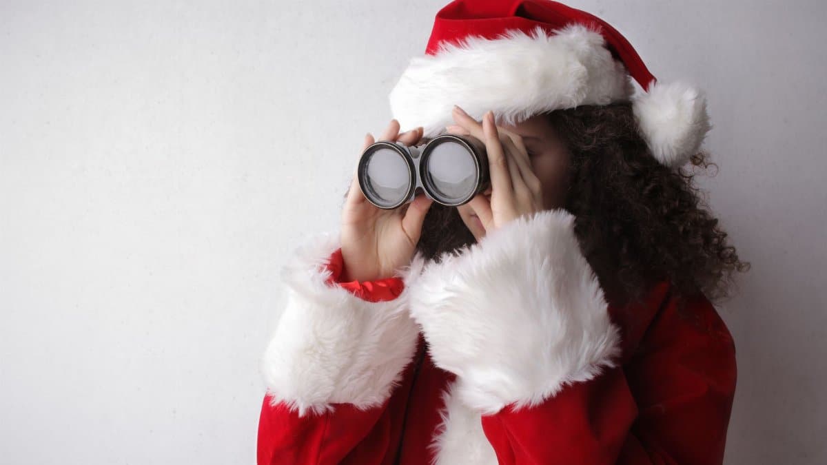 Woman in Santa outfit looking through binoculars, celebrating Christmas.