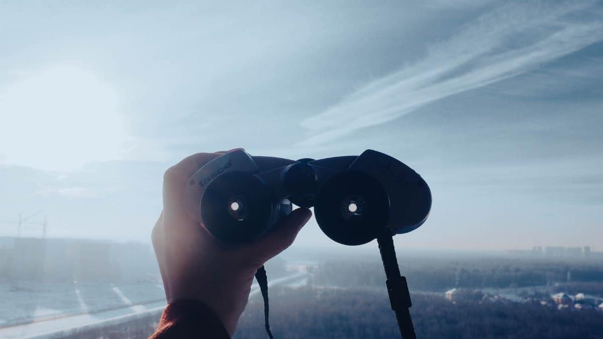 A hand holds binoculars toward a scenic horizon under a clear sky, capturing adventure and exploration.