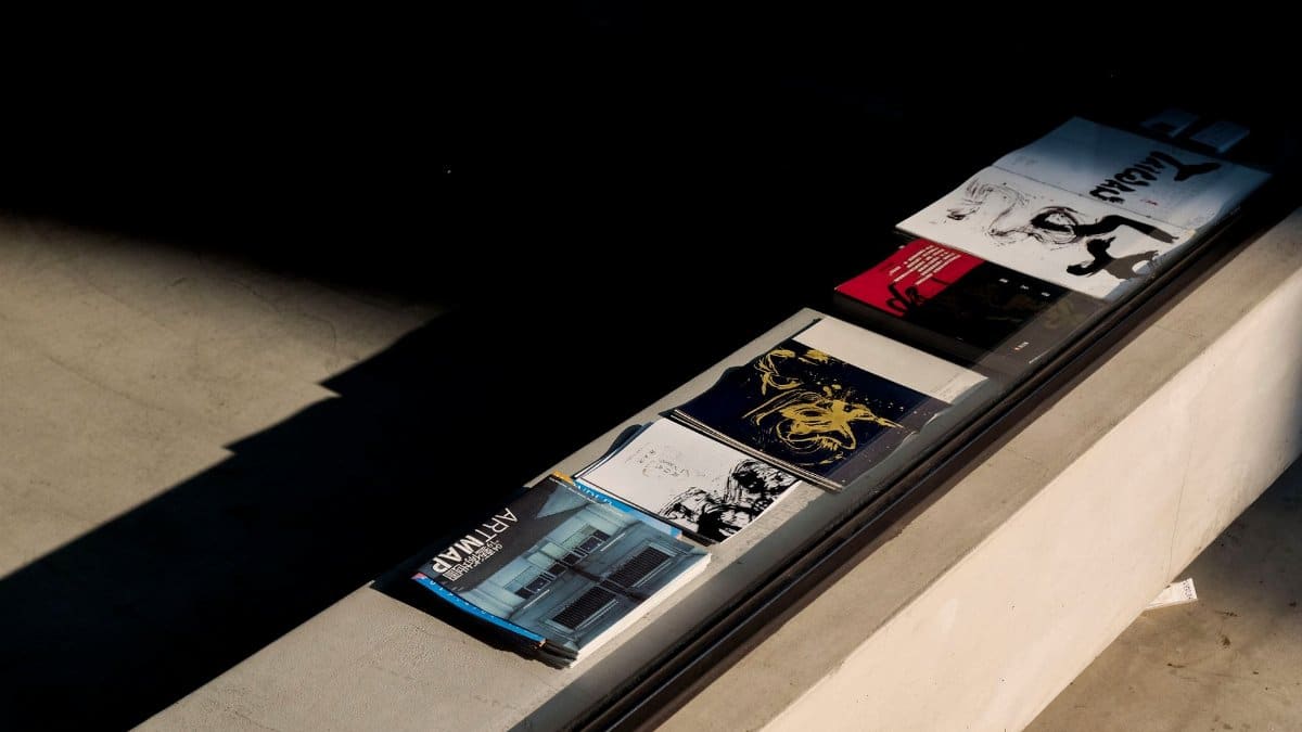 Art magazines and brochures on a sunlit concrete surface, highlighting shadow play and design.