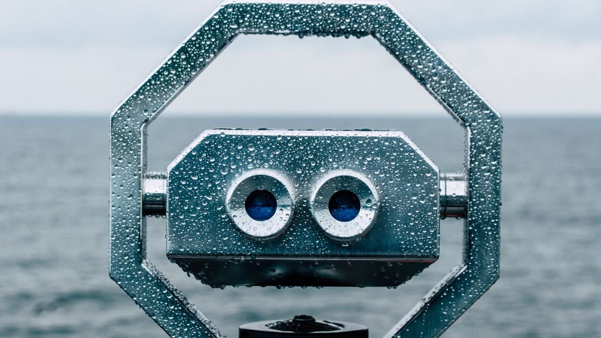Close-up of a rain-covered marine telescope facing the ocean on a cloudy day.