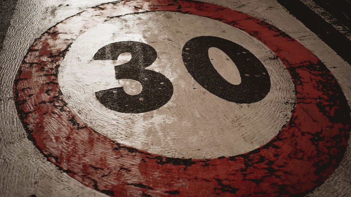 A weathered 30 speed limit sign painted on an asphalt road surface.