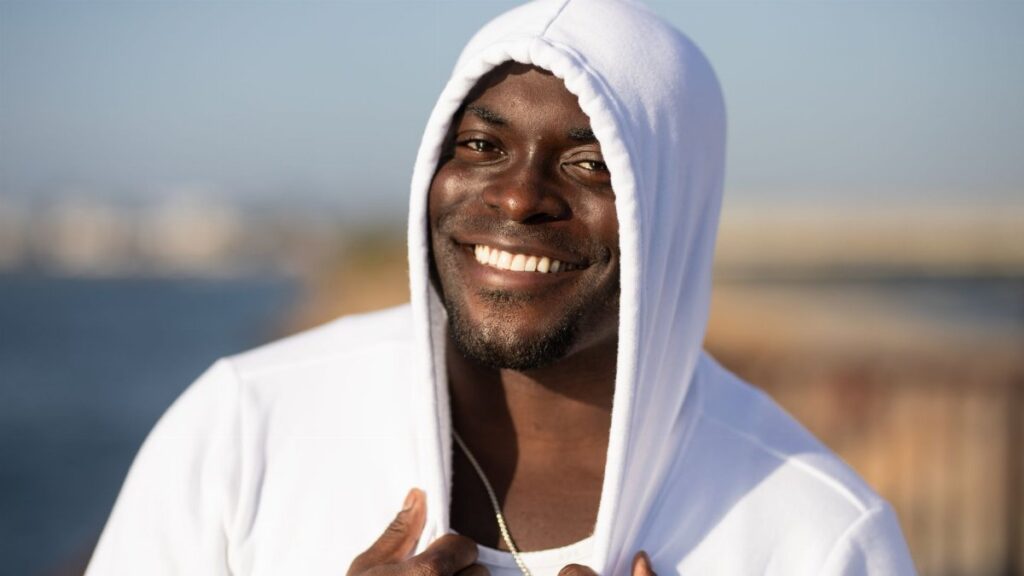 Smiling man in white hoodie enjoying a sunny day outdoors.