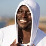 Smiling man in white hoodie enjoying a sunny day outdoors.