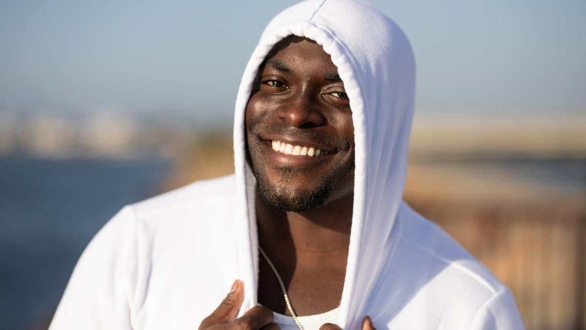 Smiling man in white hoodie enjoying a sunny day outdoors.