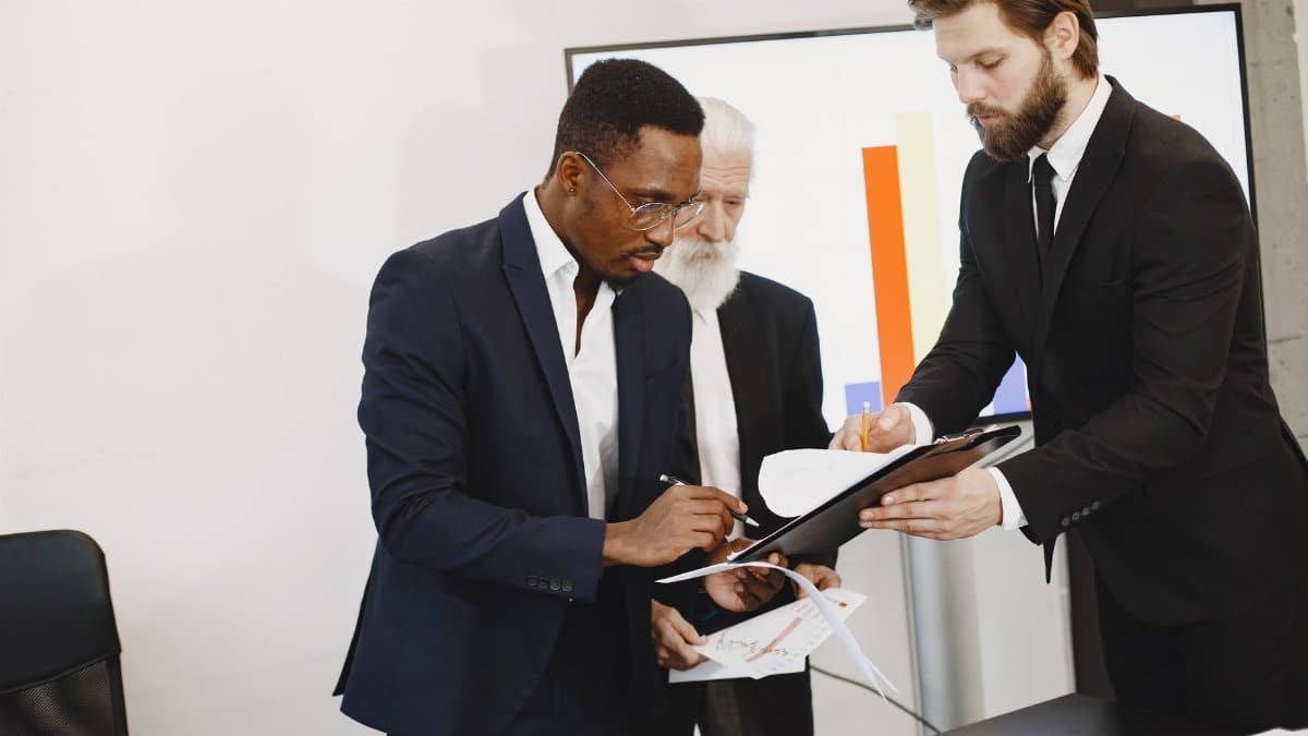 Three businessmen engaged in document signing in a modern office setting.