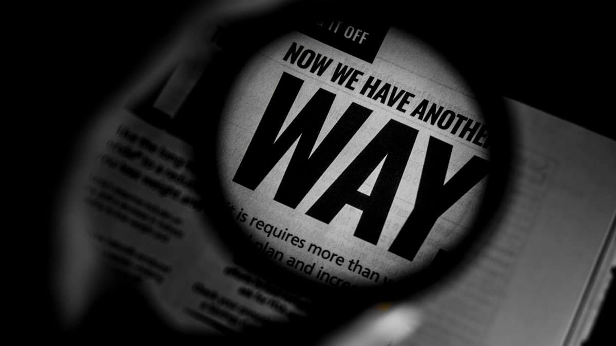 Black and white close-up of newspaper text magnified through a lens, emphasizing the word 'WAY'.