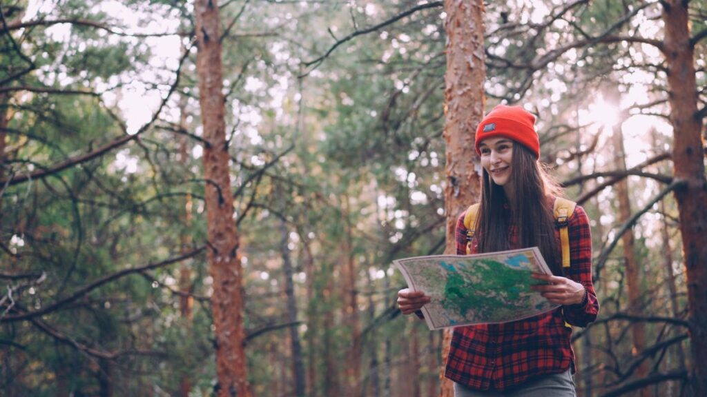 Smiling young woman in a forest holding a map, exploring nature with confidence.