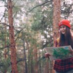 Smiling young woman in a forest holding a map, exploring nature with confidence.