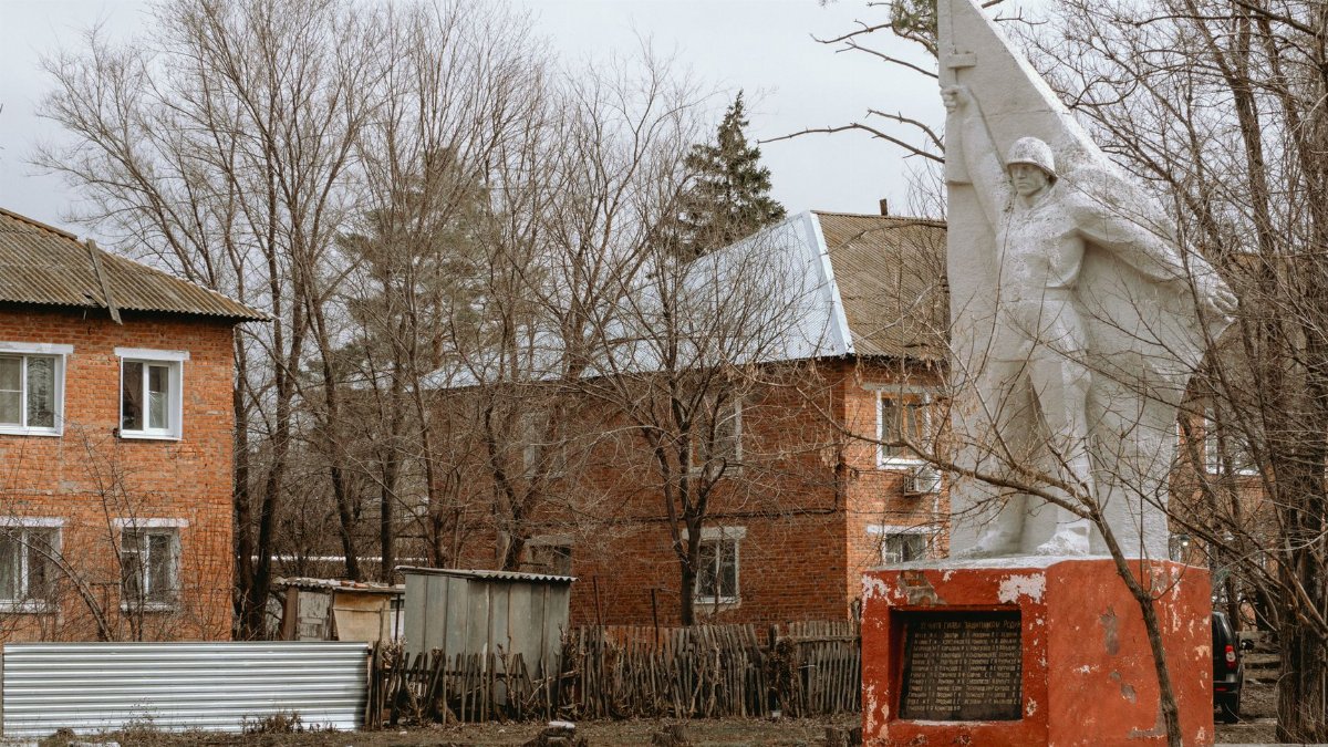 Statue of soldier in Семенной, Russia, surrounded by bare trees and houses.