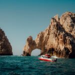 Explore the iconic El Arco rock formations in Cabo San Lucas with a boat navigating the blue Pacific waters.