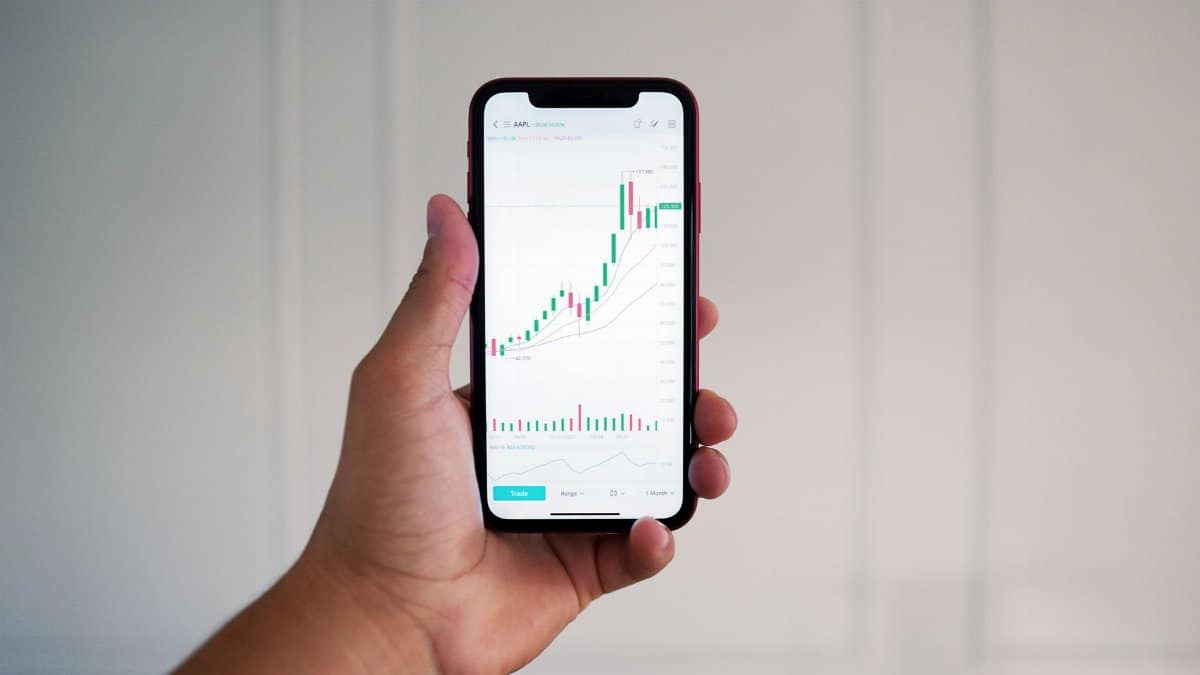 Close-up of a hand holding a smartphone showing a stock market chart indoors.