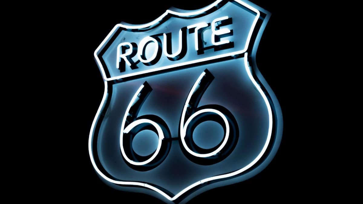 Bright neon Route 66 sign glowing on a black background, vintage style.